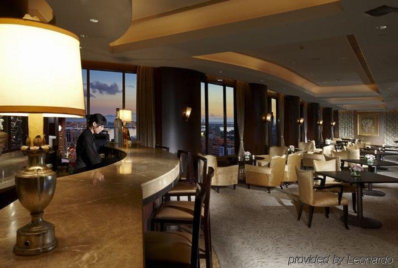 Ambassador Hotel Kaohsiung Restaurant foto The photo depicts an elegant bar or lounge area within a high-rise setting. The interior features warm lighting, with a large lamp illuminating the bar counter. There is a bartender seated at the bar, and the space includes plush chairs and tables ar