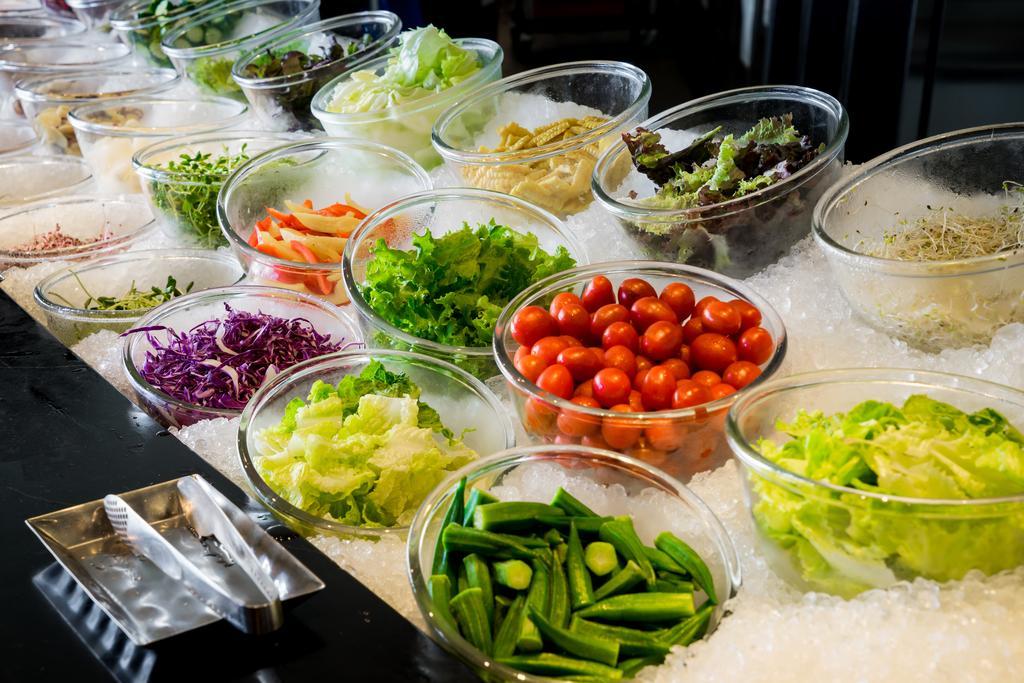 Ambassador Hotel Kaohsiung Buitenkant foto The photo displays a vibrant array of fresh vegetables and greens arranged in clear bowls on a bed of ice. The selection includes various leafy greens, chopped vegetables, and colorful ingredients. There are items like cherry tomatoes, purple cabbage