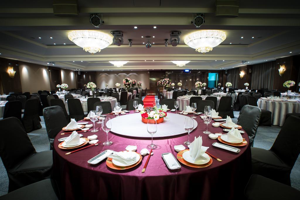 Ambassador Hotel Kaohsiung Buitenkant foto The photo depicts an elegantly set dining area for an event. 

In the foreground, there is a circular table covered with a dark red tablecloth, featuring a centerpiece of flowers in vibrant colors. The table is equipped with white plates, polished cu