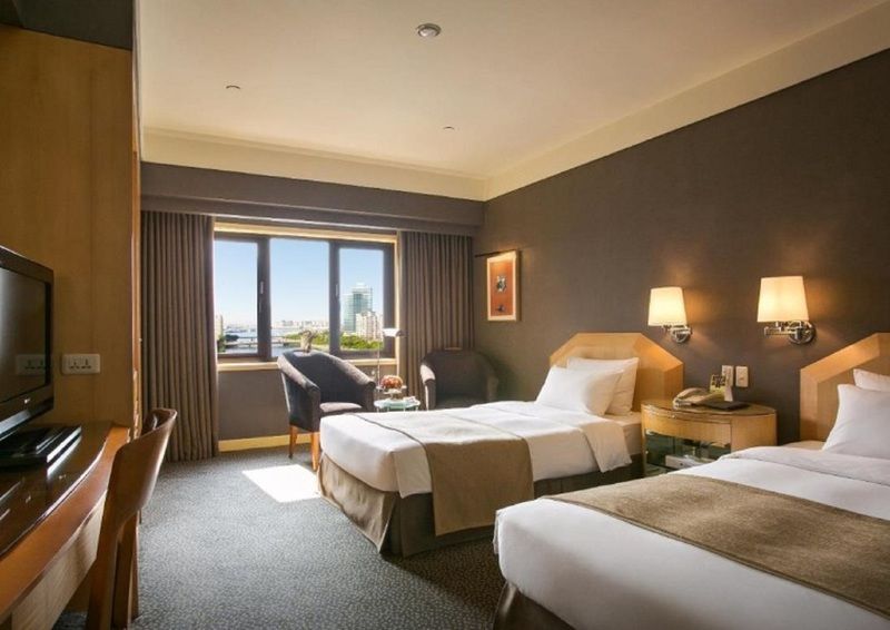 Ambassador Hotel Kaohsiung Buitenkant foto The photo shows a hotel room featuring two twin beds with beige and brown bedding. The room has a modern design with a dark accent wall and light-colored furniture. There are bedside lamps on each side of the beds, and a comfortable armchair is posit