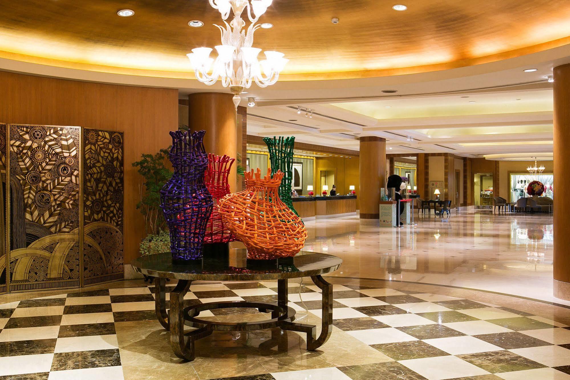 Ambassador Hotel Kaohsiung Buitenkant foto The photo shows the interior of a hotel lobby featuring an elegantly designed space. In the foreground, there is a decorative table with colorful woven vases, predominantly in purple and orange. These vases add a vibrant touch to the setting. The flo