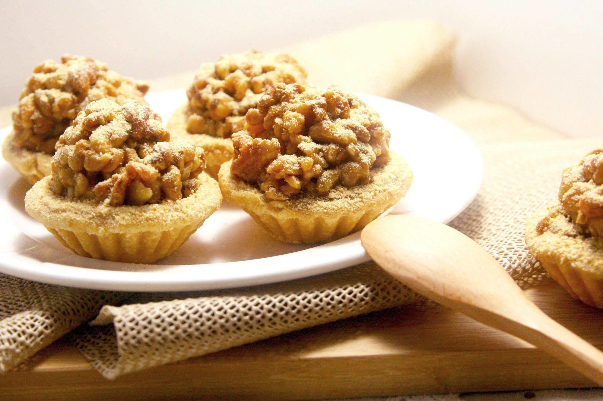 Ambassador Hotel Kaohsiung Buitenkant foto The photo shows a plate with small, dessert-like tarts. Each tart features a golden, crumbly crust that is filled with a mixture of chopped nuts and a sweet topping, likely caramelized for added flavor. The tarts are arranged neatly on a white plate,