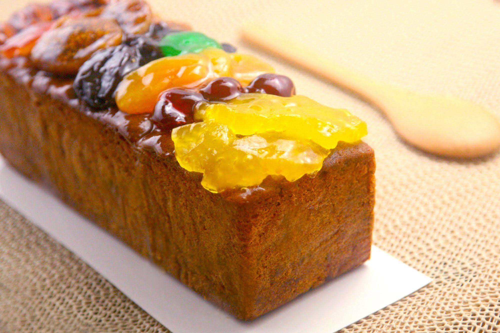 Ambassador Hotel Kaohsiung Buitenkant foto The photo shows a rectangular fruitcake that has a rich, dark color and is topped with an assortment of candied fruits. The toppings include brightly colored fruits like orange, green, and yellow, arranged attractively on top of the cake. The texture