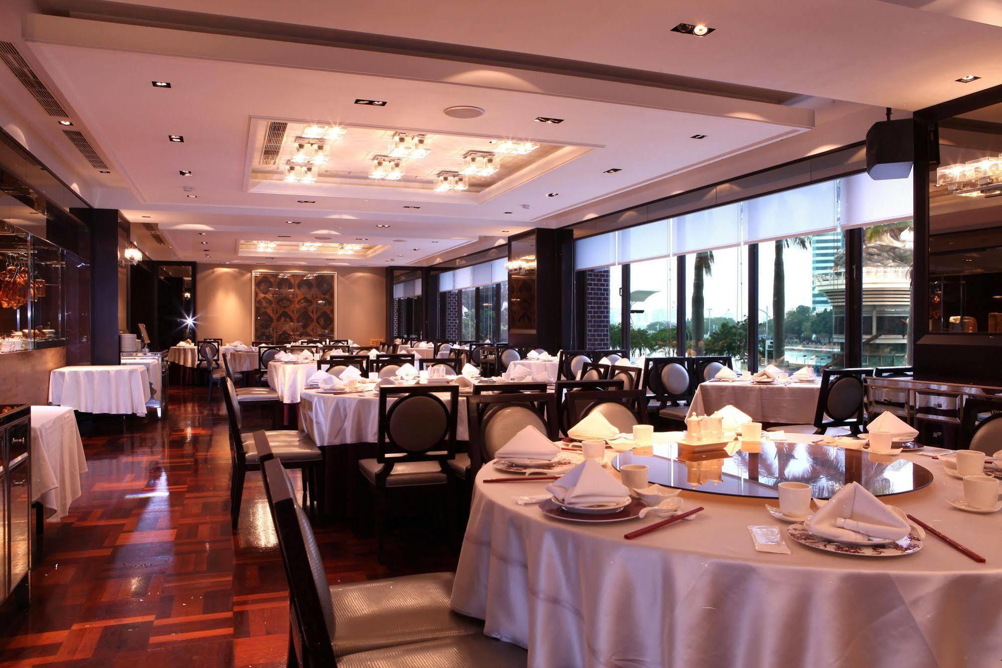 Ambassador Hotel Kaohsiung Buitenkant foto The photo shows an elegant restaurant interior. It features neatly arranged tables with white tablecloths and dining settings, including plates, cutlery, and folded napkins. The space is well-lit with ambient lighting and large windows that likely pr