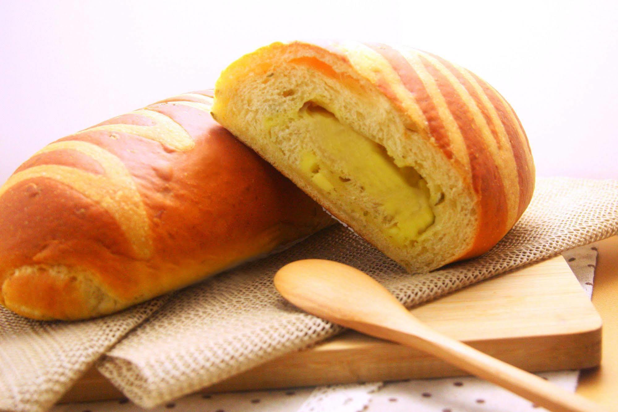 Ambassador Hotel Kaohsiung Buitenkant foto The photo shows a loaf of bread that has a golden-brown crust with striped patterns on its surface. One loaf is partially sliced open, revealing a soft, yellow filling inside, which suggests that it might be flavored or sweetened. The bread is placed