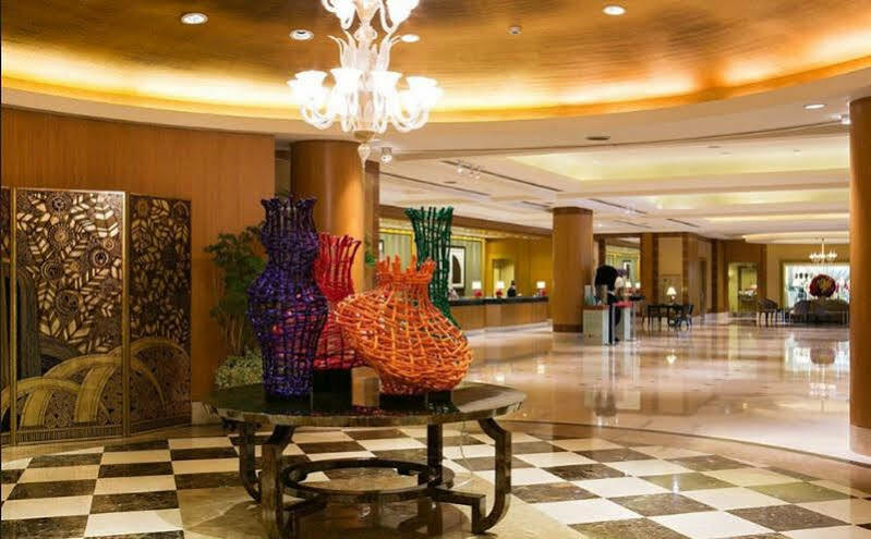Ambassador Hotel Kaohsiung Buitenkant foto The image shows a spacious and elegantly designed lobby area. In the center, there are several large, artistic vases made of colorful materials, including shades of purple, orange, and green. These vases are displayed on a black table, contrasting wi